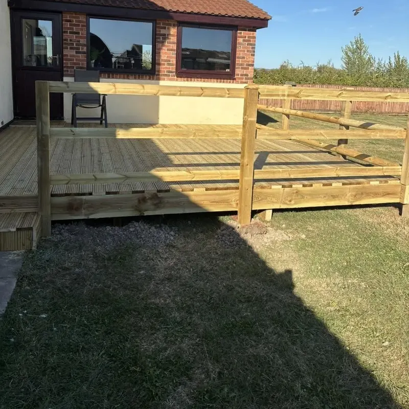 A finished raised timber deck with rails and a step, beside a brick house