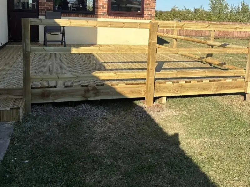 A finished raised timber deck with rails and a step, beside a brick house