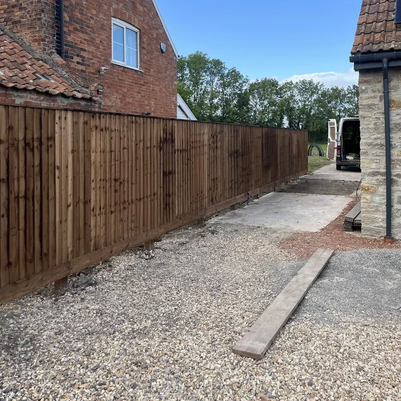 A new closeboard fence along a gravel drive beside a brick house