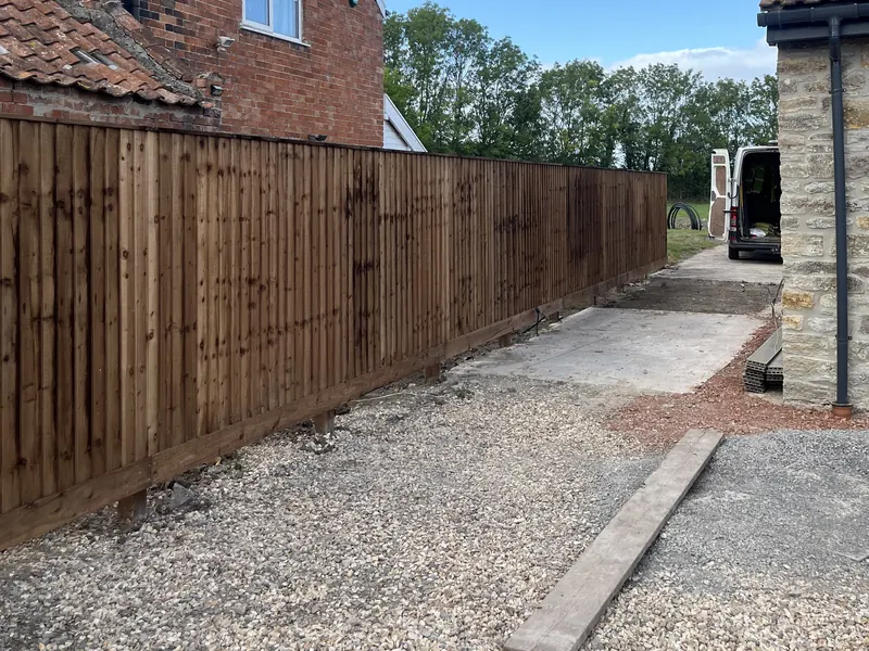 A new closeboard fence along a gravel drive beside a brick house