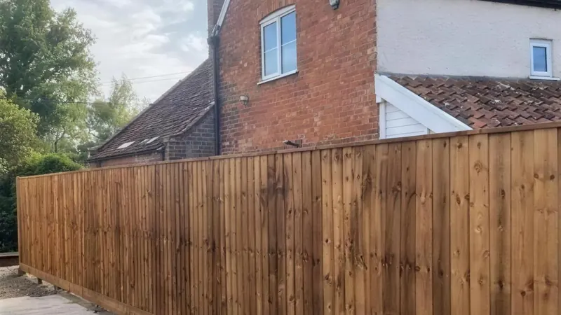 A new closeboard boundary fence along a drive, a cottage behind