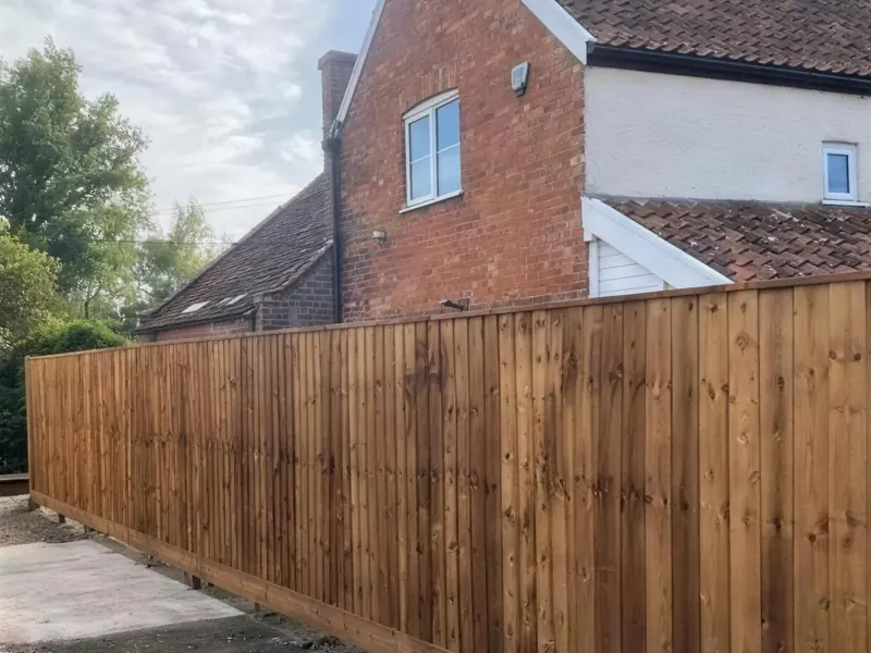 A new closeboard boundary fence along a drive, a cottage behind