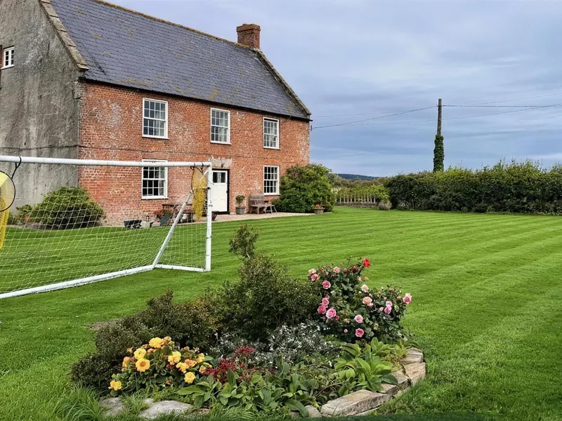 A striped lawn in front of a red-brick farmhouse, a flower bed beside it