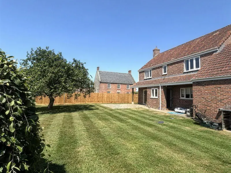 A large lawn mowed into stripes beside a red-brick house