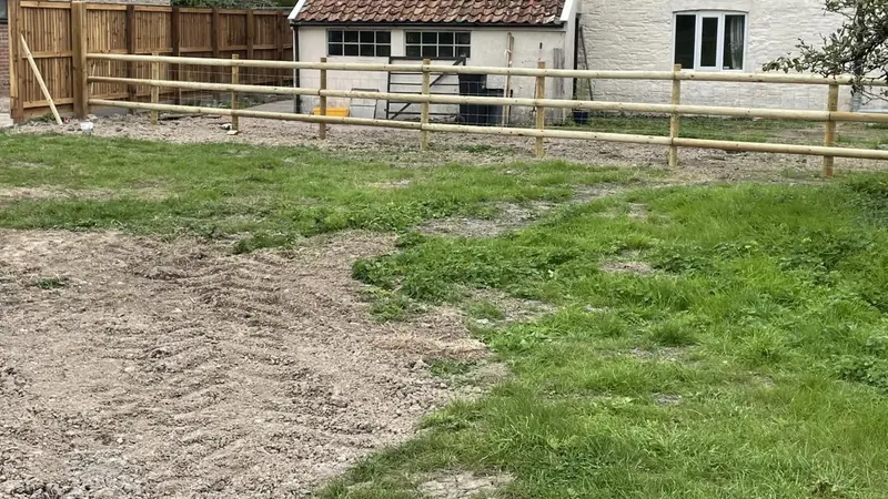 Post and half-round rail fencing with stock wire across an open paddock