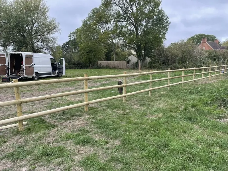 A long post and rail fence running across a field, trees beyond